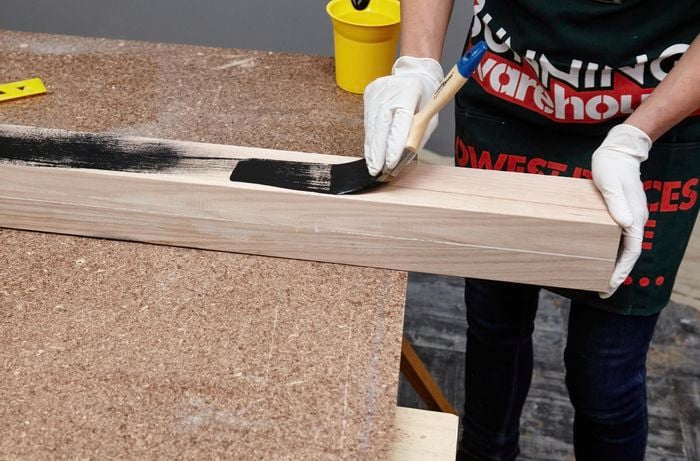 Two lengths of timber being painted black by a Bunnings team member