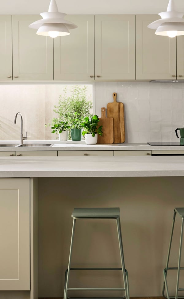 Light green modern kitchen with a white benchtop, green bar stools at the benchtop and white drop down lights.