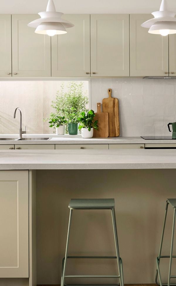 Light green modern kitchen with a white benchtop, green bar stools at the benchtop and white drop down lights.