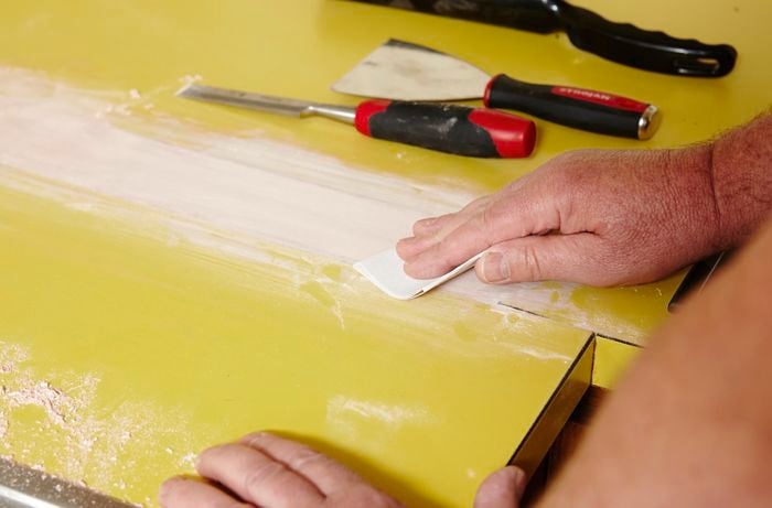 Person sanding benchtop after using putty on it.