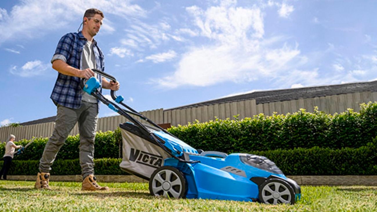 A man using a Victa lawn mower to mow the lawn.
