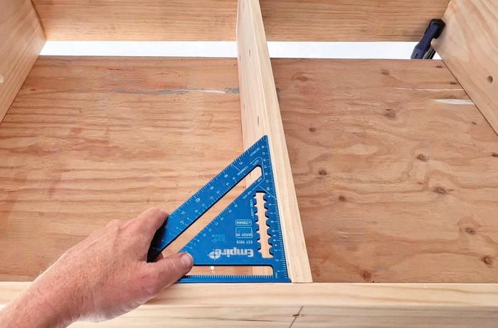 Hand using rafter square to check the top and base are straight against sides.