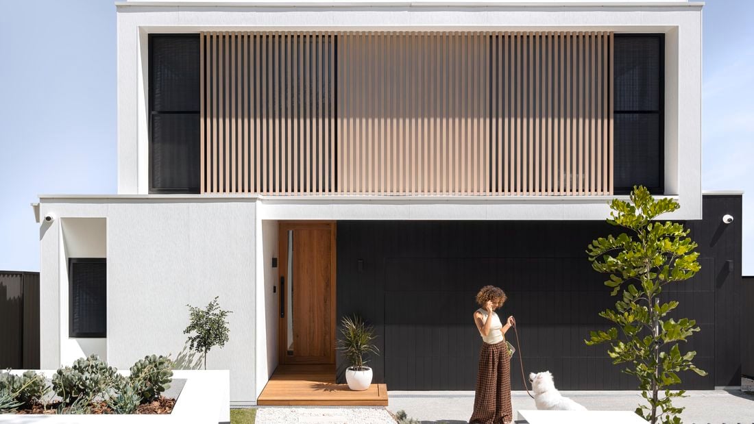 Front yard view of white and black exterior house with woman holding dog on a leash.