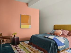 A stylised bedroom with a feature wall painted in Dulux’s baked clay, a bed and rug in on-trend colours.]