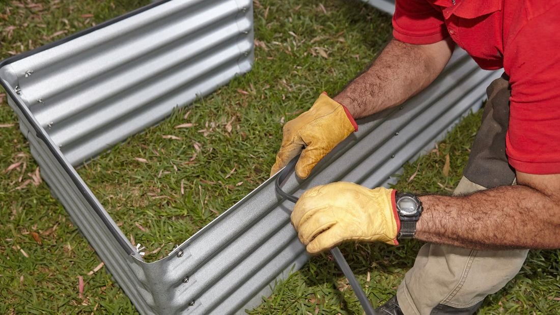 Person sticking protective edging to corrugated iron garden bed.