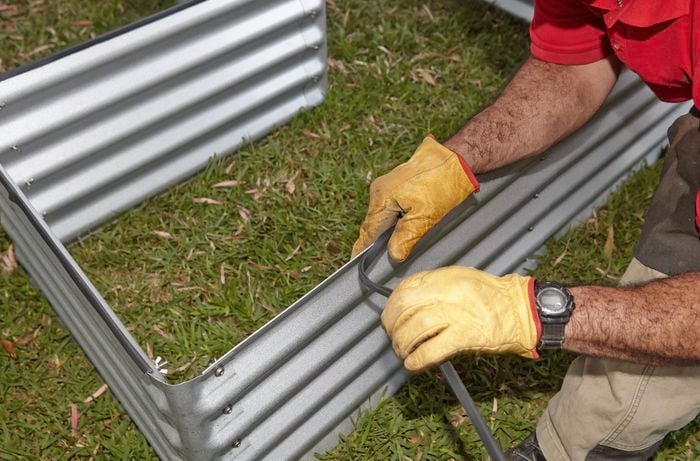 Person sticking protective edging to corrugated iron garden bed.