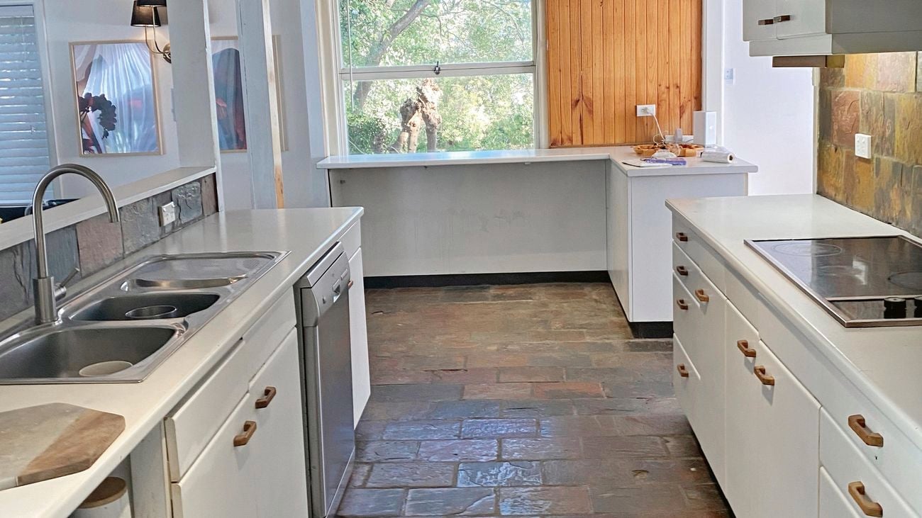 70's style warm toned kitchen with outdated cabinetry and the same large block tiles on the floor and the splashback