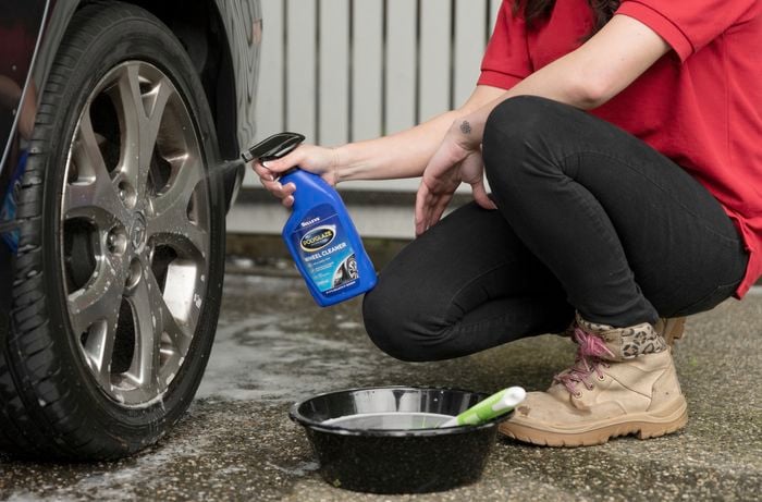 A person seated and applying Selleys Polyglaze wheel cleaner to the car wheel. ]