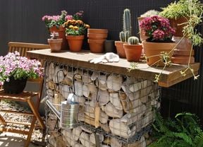 A completed gambion potting bench with trowel, stainless steel watering can and several potted succulents on top