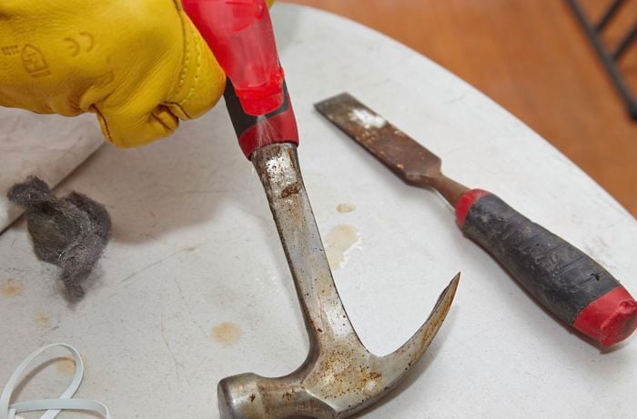 A person spraying a rusty hammer with an abrasive chemical
