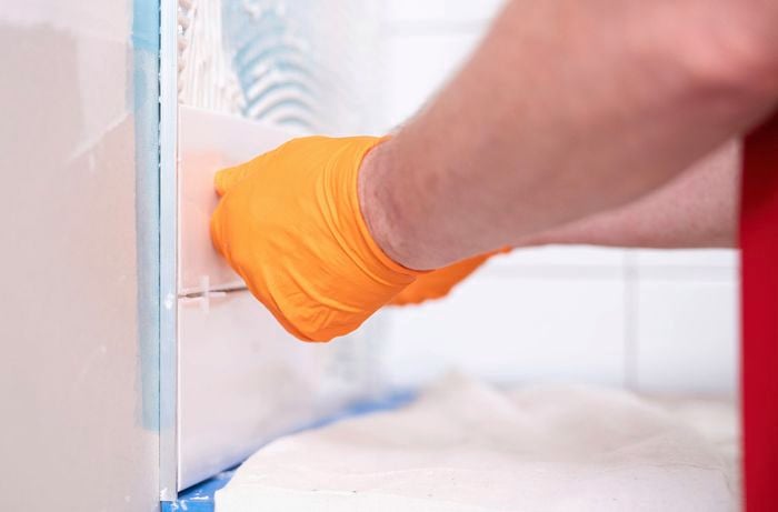 A person wearing orange gloves is installing the tile trim into the adhesive to hold it securely in place.  ]