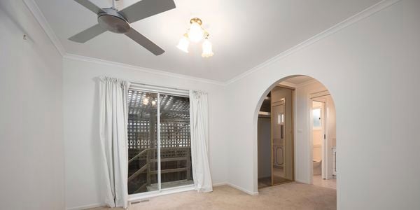 A room with carpet on the floor, ceiling fan, an archway and a glass sliding door to outside