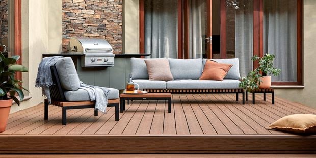 A Barbecue and outdoor setting on a timber decking with a cushion and pot plants on it.