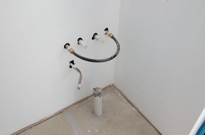 Capped water pipes and taped off power leads protruding from holes in a laundry wall