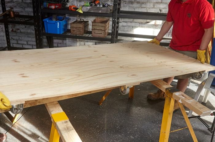 A flat panel of timber with six castor wheels attached to the underside being positioned on a workbench