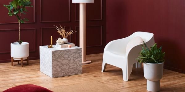 A lounge room with a chair, pot plants, lamp and table in it.