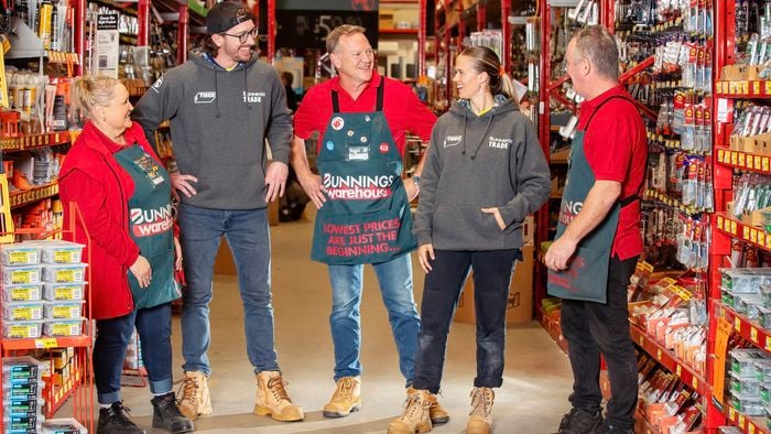 Five Bunnings team members standing together in a store aisle, talking amongst themselves stocked with hardware products.