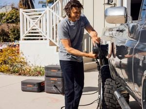 A man uses a portable car polisher outside which is plugged into a Jacker portable power station.