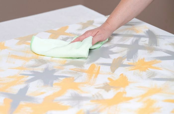 : A person is gently wiping a canvas surface using a soft microfibre cloth to remove dust.