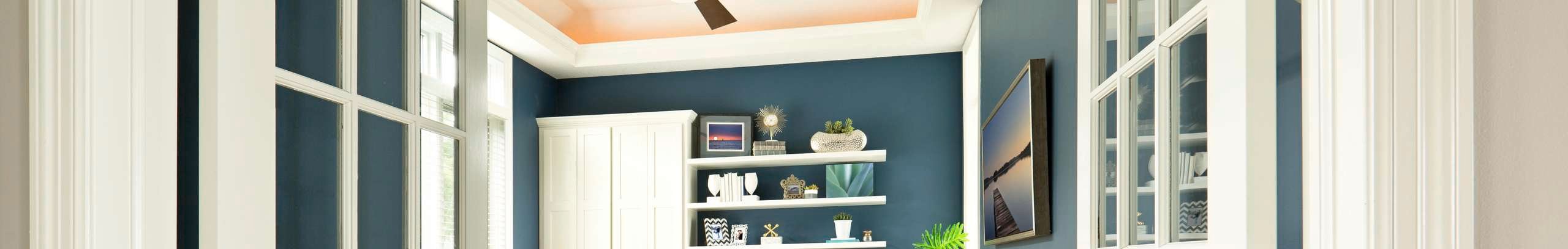 Contemporary study/office space featuring blue walls, timber built-in desk and a black ceiling fan