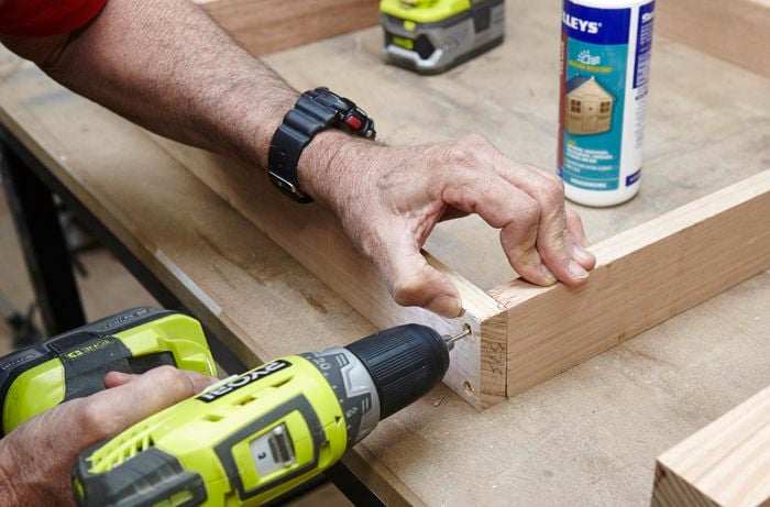 The subframe of an outdoor wooden table being screwed into place with a power drill