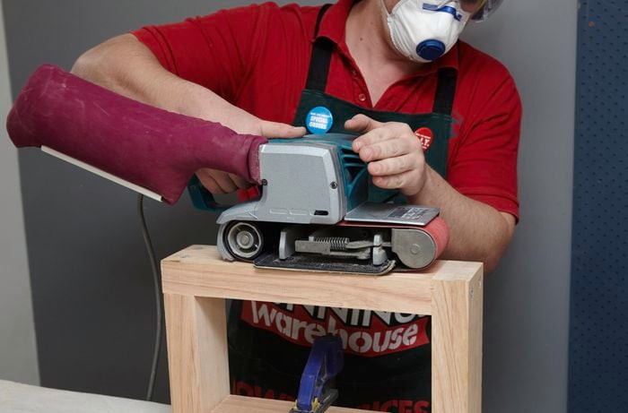 A person sanding a timber rectangle using a belt sander