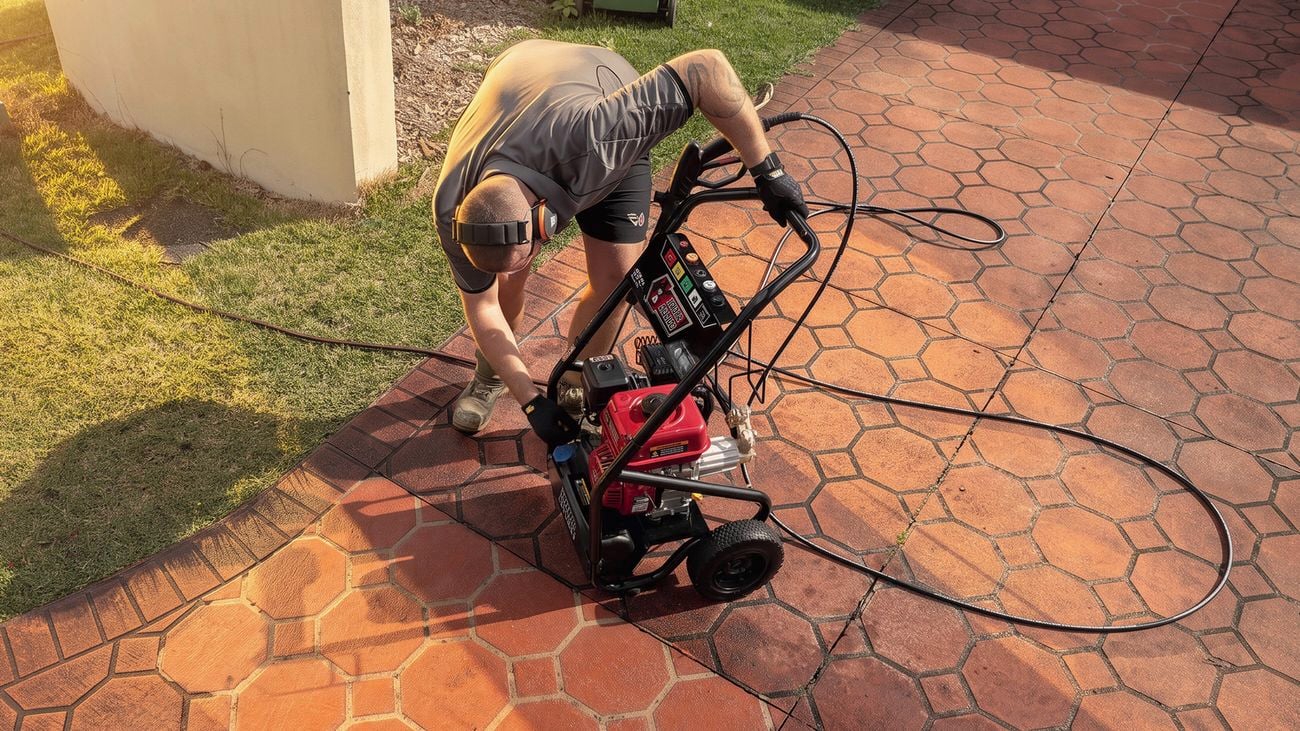 Person connecting or adjusting a pressure washer on a paved driveway before cleaning.