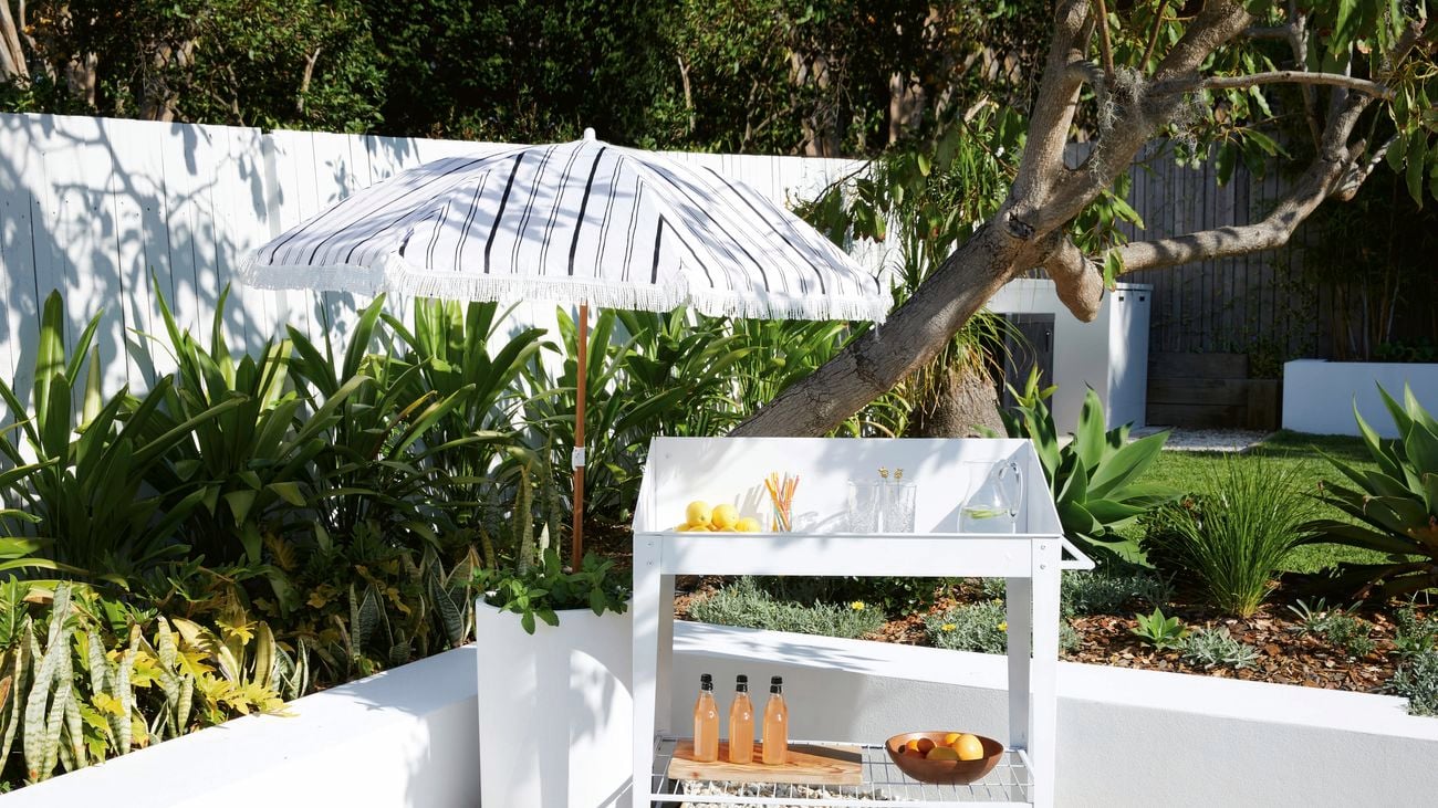 A white, drinks trolley set up outside with drinks and glasses on both levels.