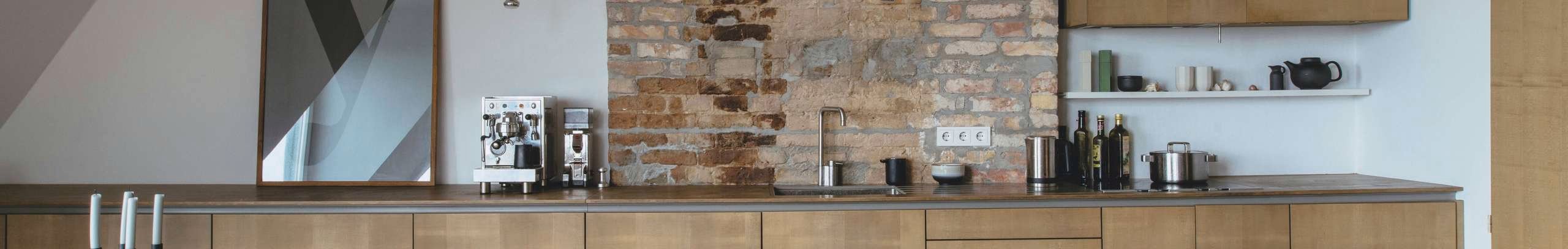 Modern open planned kitchen with timber look cabinetry and exposed brick wall.