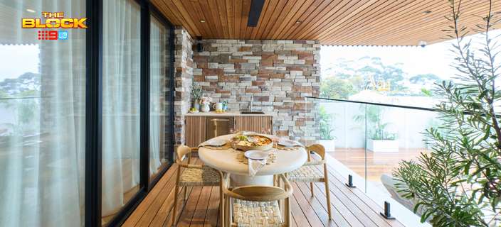 Covered outdoor dining area featuring timber decking and ceiling, a dining table, stone feature wall and glass balustrade.