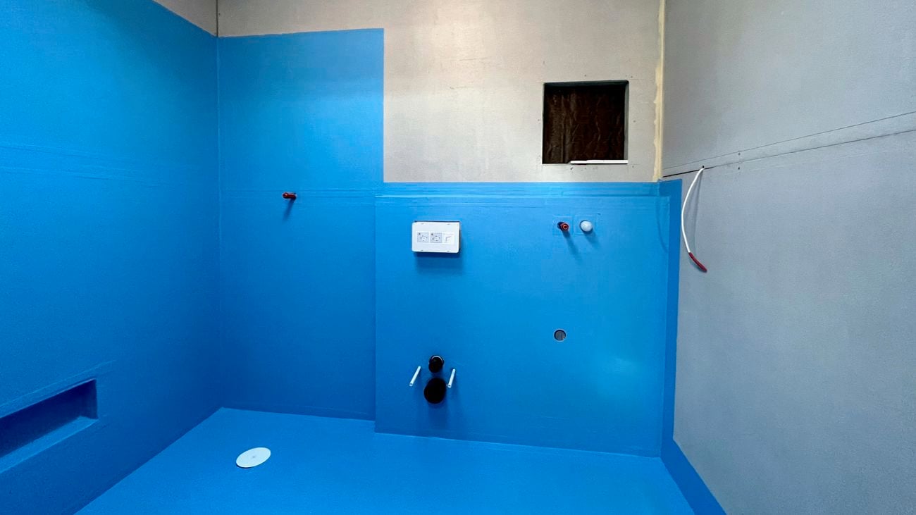 Empty bathroom under renovation with blue waterproofing along the walls and floors.