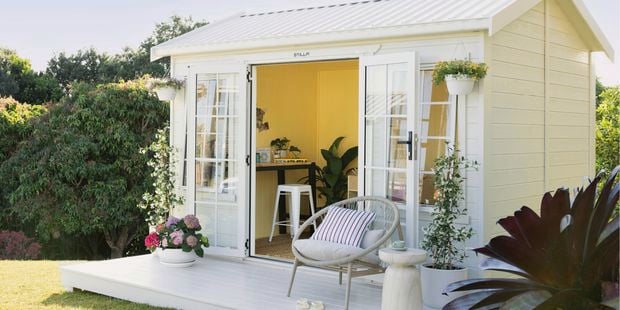 Front of a small creative studio styled with a chair and pots with flowers.