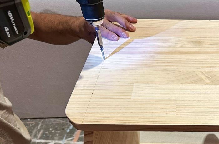 A hand uses a drill to screw panels together for a timber coffee table