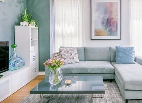 Living room featuring a light blue sectional sofa, dark grey coffee table with flowers, and large framed artwork on the wall.
