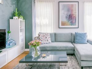 Living room featuring a light blue sectional sofa, dark grey coffee table with flowers, and large framed artwork on the wall.