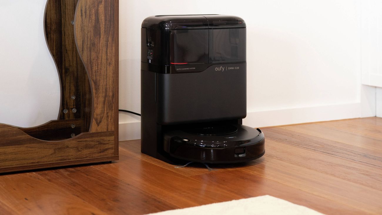 Robot vacuum docked at a charging station beside a wooden cabinet.