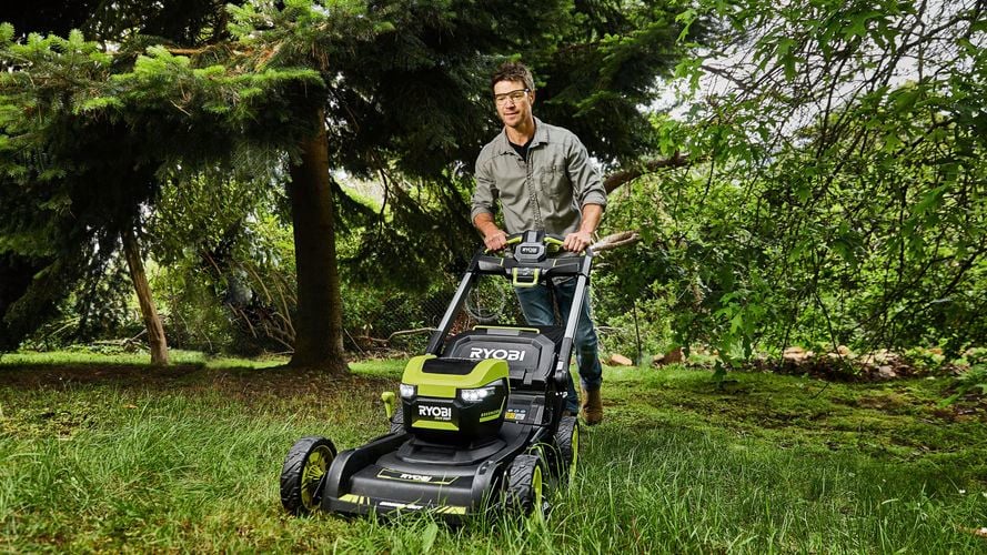 A person wearing protective gear and operating a lawn mower to cut the grass on a garden. 