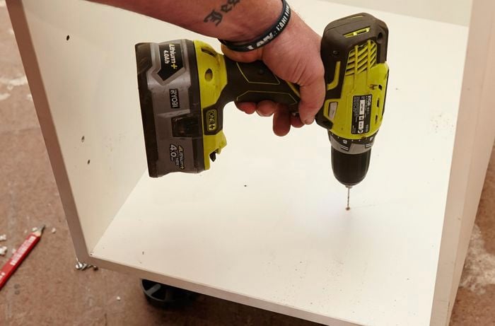 Person drilling holes into base of cabinet
