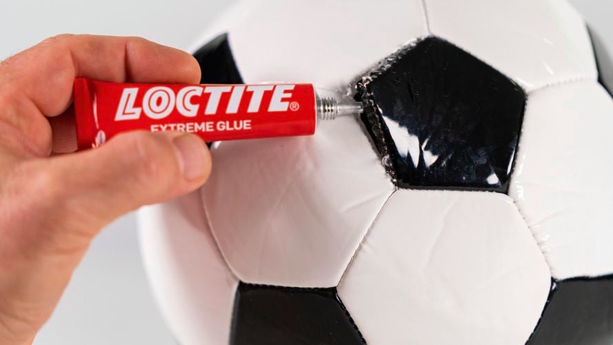 Person repairing broken soccer ball with Loctite Extreme Glue.
