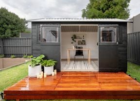 A finished backyard shed, painted black and with a wooden stained deck