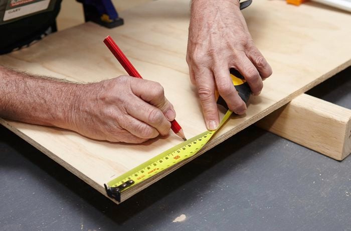 A person marking length on timber panel using measuring tape and pencil