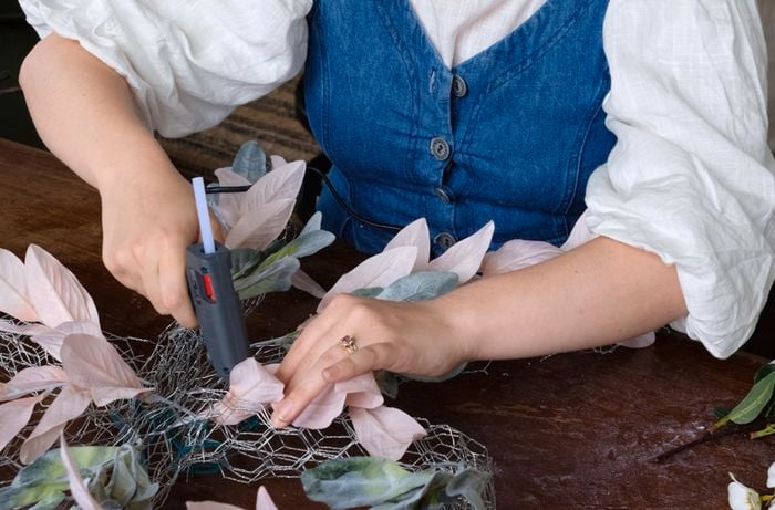 Lady hot gluing artificial flowers to wire bow.
