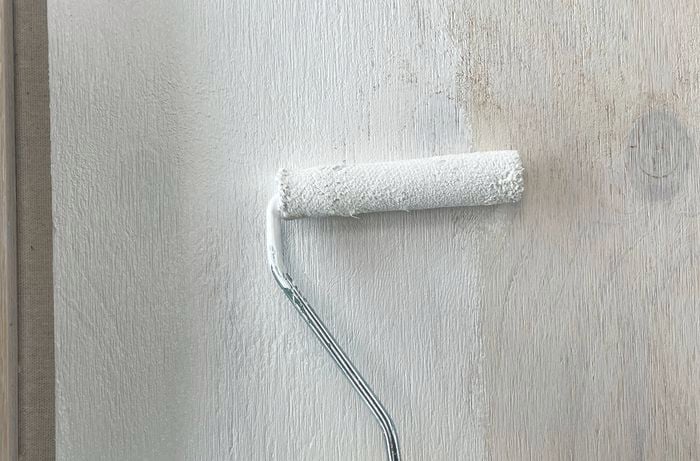 A hand using a paint roller to apply primer to cut pieces of plywood