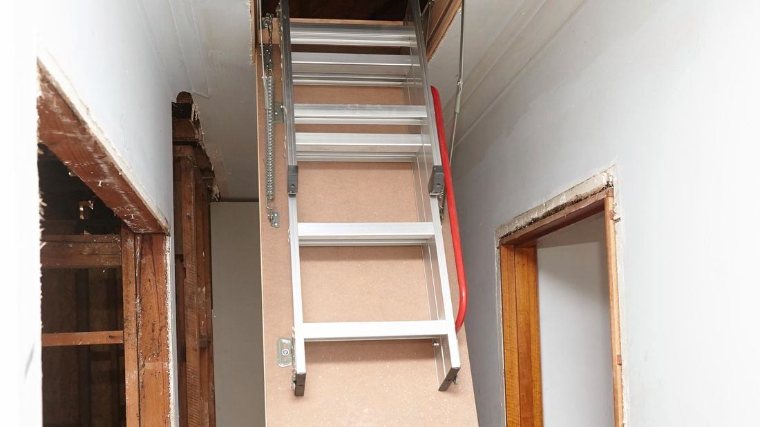 An attic ladder ascending into a ceiling in a hallway