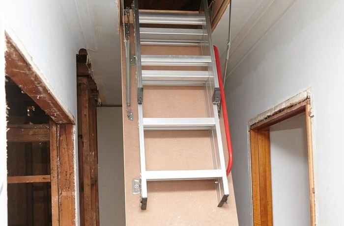 An attic ladder ascending into a ceiling in a hallway