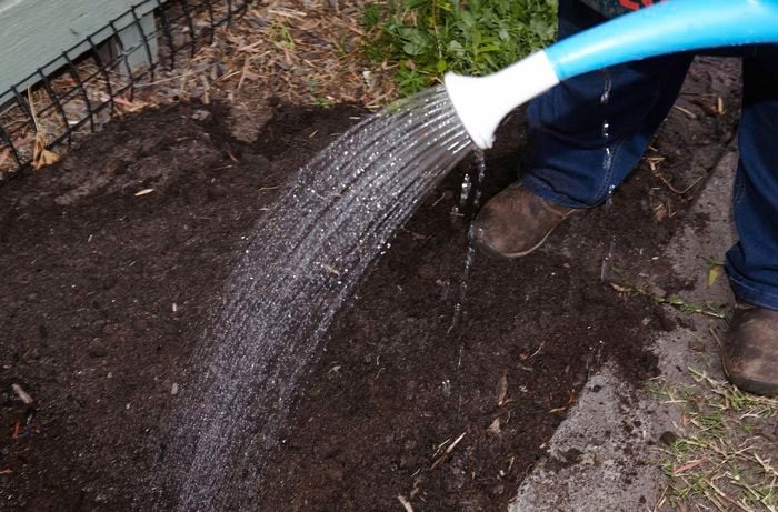 A person watering a garden bed using a watering can