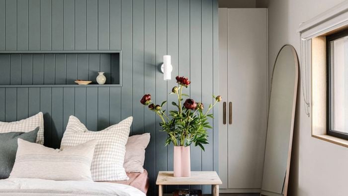 A bedroom with a bed, bedside table with a case on it, mirror and a cupboard in it.