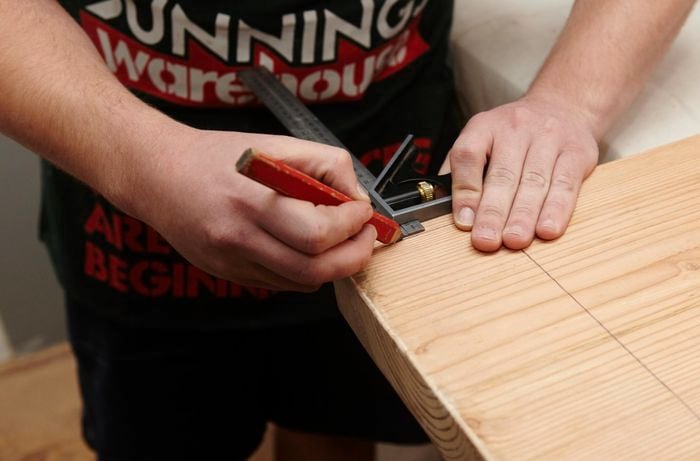 A person marking the corner of a piece of timber using a set square