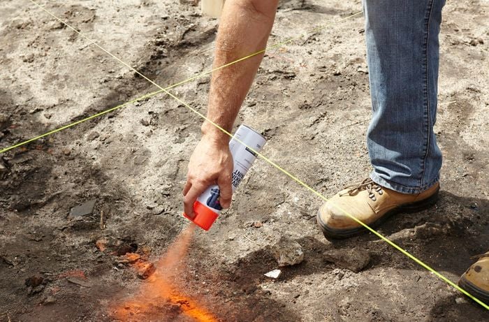An orange paint spray can being used to mark bare earth for a foundation dig site