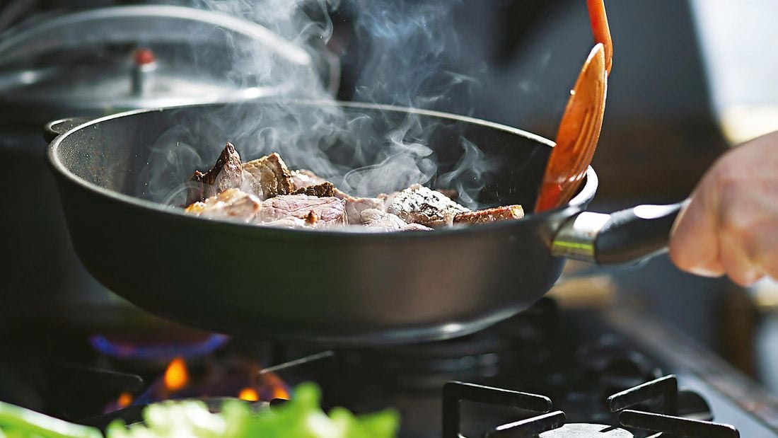 Close up of a hot pan cooking steak on a high heat.